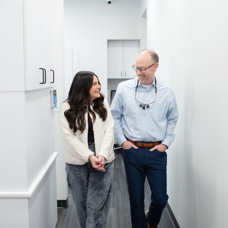 Dr. Hoftiezer walking down a hallway with a smiling patient, both engaged in friendly conversation inside a bright, modern dental office.