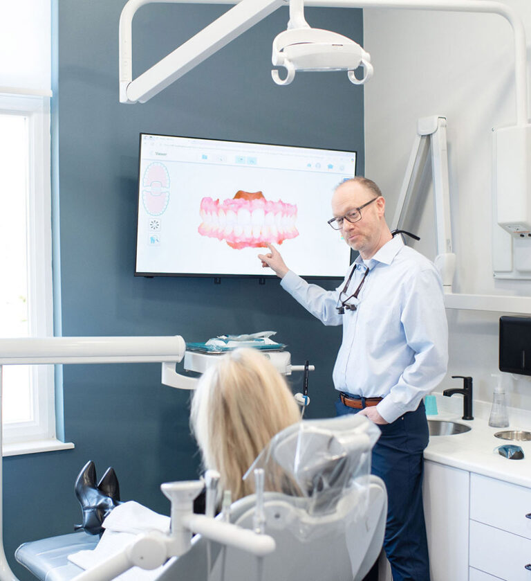 Dr. Hoftiezer pointing at a dental scan displayed on a screen while discussing treatment with a patient seated in the dental chair in a modern exam room.